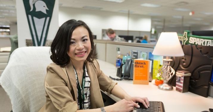 Supply chain grad Xuesi Li sits at her desk that's adorned with Michigan State University merch.