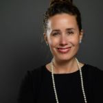 Elizabeth Blass, graduate of the Master of Science in Management, Strategy and Leadership program, smiling in front of a black backdrop wearing a black shirt and pearl necklace.