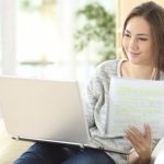 A woman using a laptop and spiral notebook with handwritten notes determining if a graduate certificate is worth it.