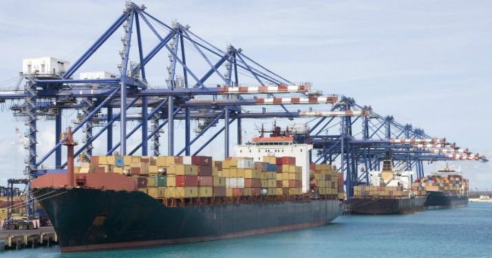 Large cargo ship at a U.S. port with shipping containers being loaded by cranes.