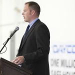 Garrett Stricker speaking at a podium wearing a suit and tie.