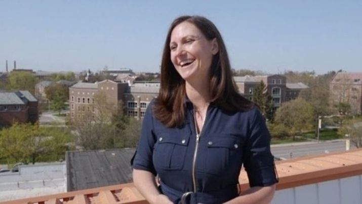 Jennifer Wolf, Management, Strategy and Leadership grad, being interviewed on a rooftop with a panoramic view of the buildings behind her.