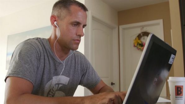 Mark Thompson, Management, Strategy and Leadership grad, using a laptop wearing an MSU T-shirt and white earphones.