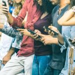 Millennials leaning against a wall using smartphones.