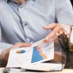 Close up shot of sitting at a desk holding a piece of paper with bar charts on it.