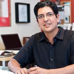 A man sitting at his desk in an office, smiling and talking about leadership.