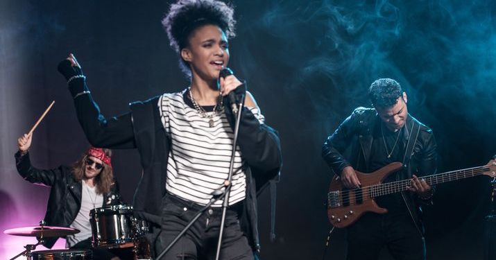 Band playing on a smoky, dark-lit stage with a singer, drummer and bass player.