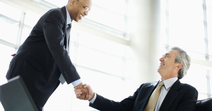 Two business men in a lobby shaking hands after a successful negotiation.