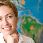 Woman with a yellow pencil behind her ear smiling into the camera in front of a world map.