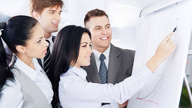 Group of four coworkers looking at a large sketch pad while one woman finishes drawing an upward-trending line graph.