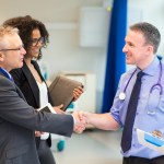 Healthcare professionals meeting with a doctor, shaking his hand and introducing themselves.