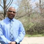 Ramar Scales, MS in Management, Strategy and Leadership grad, smiling in front of a forest.