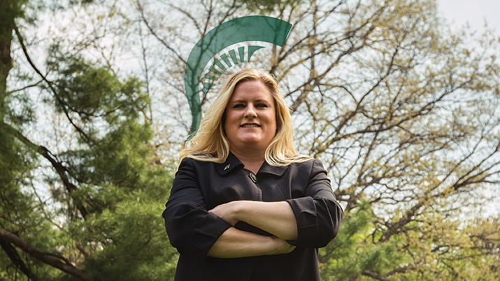 Heather Serrano, graduate of MSU's MS in Management, Strategy and Leadership program, smiling with her arms crossed and a graphic spartan helmet above her head.