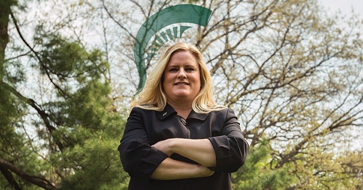 Heather Serrano, graduate of MSU's MS in Management, Strategy and Leadership program, smiling with her arms crossed and a graphic spartan helmet above her head.