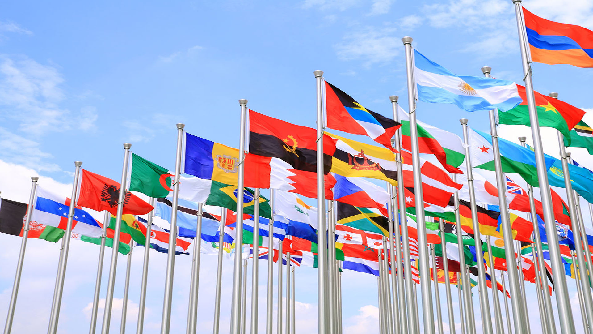 Flags from countries all over the world waving in the breeze against the backdrop of a blue sky.