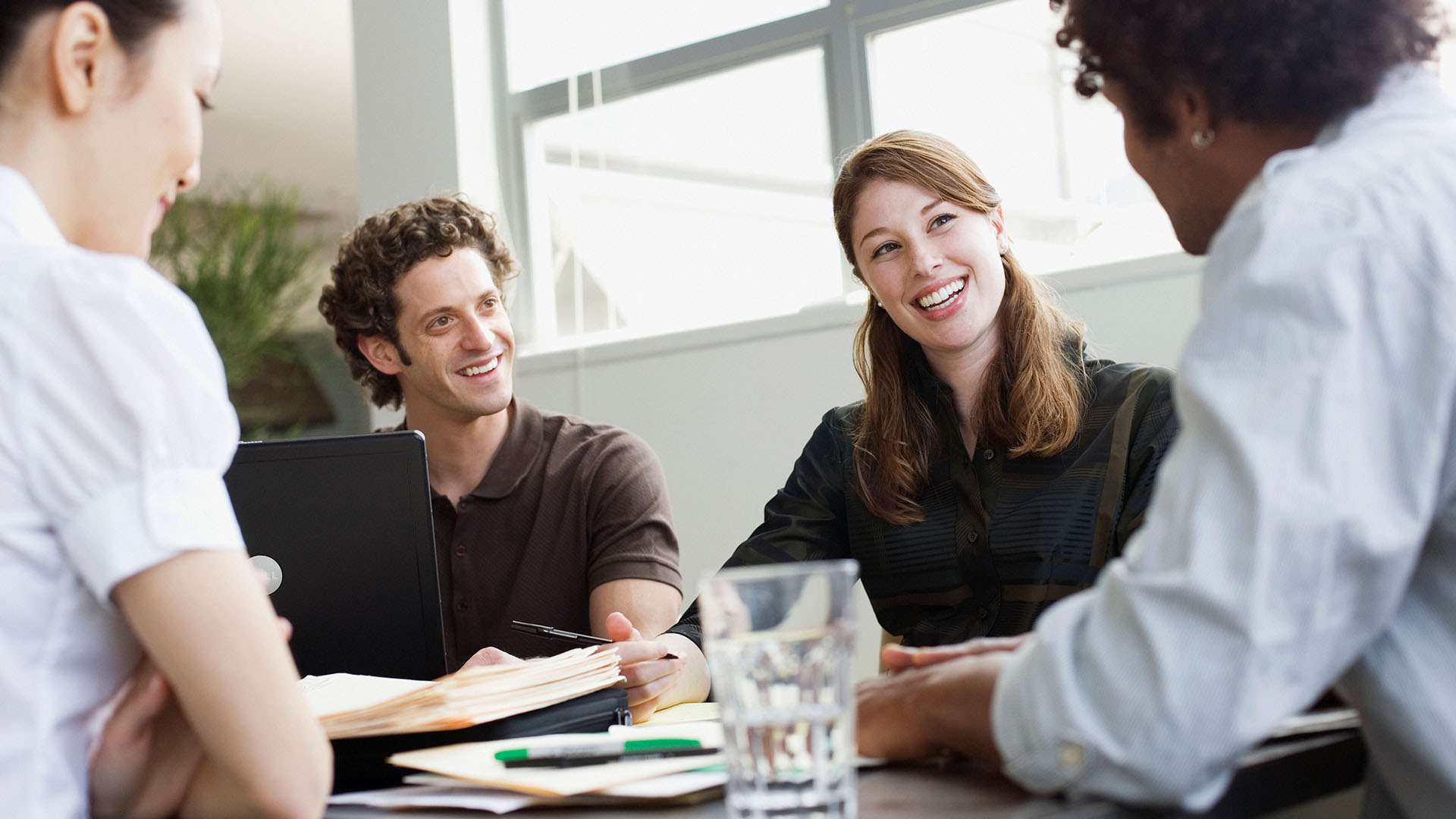 A group of employees sitting around a table with glasses of water and notebooks talking about leadership.