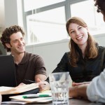 A group of employees sitting around a table with glasses of water and notebooks talking about leadership.