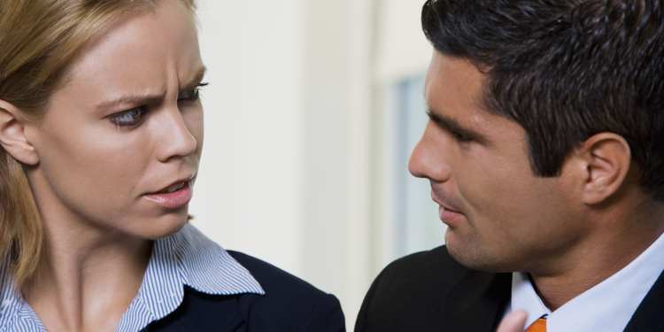 Man and woman in business clothes looking at each other with confused expressions, discussing the proper ethical response they should take with a situation at their workplace.