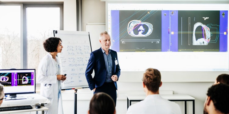Physician and healthcare administrator presenting concepts via whiteboard and computer projection to medical staff at hospital.