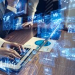 Business professionals working at computers with all manner of data analytics dashboards in a blue overlay over their work.