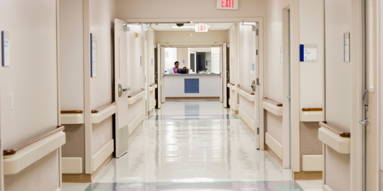 Empty hospital hall leading towards ward reception desk.